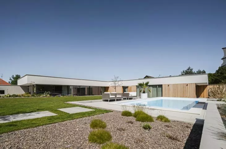 Modern L-shaped house of concrete and wood against the background of a green garden