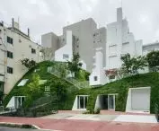 A view of a green hill covered with grass, trees and bushes, from which white geometric objects resembling simplified houses emerge