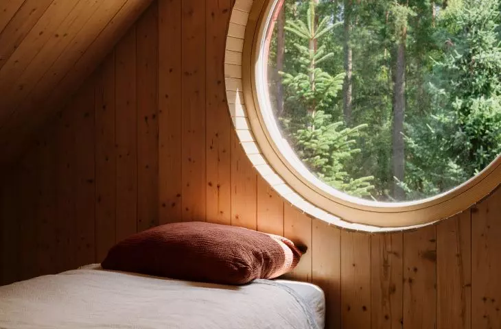 A circular window on the mezzanine frames a picturesque view of the forest