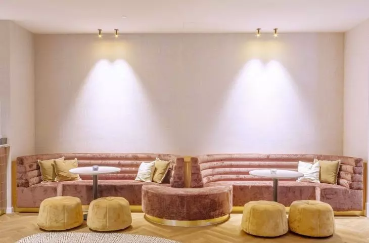 The undulating shapes of Eleganza acoustic ceilings by Knauf Ceiling Solutions harmonize with the shapes of the reception area, while plush, soft sofas in gold and pink colors enhance the effect of friendly acoustics and relaxation 