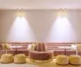 The undulating shapes of Eleganza acoustic ceilings by Knauf Ceiling Solutions harmonize with the shapes of the reception area, while plush, soft sofas in gold and pink colors enhance the effect of friendly acoustics and relaxation 
