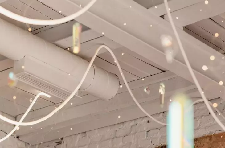 techniczny charakter sufitu przełamuje ozdobne oświetlenie — wiszące lampki przypominające diamenciki, odbijające światło kryształki i świetliste girlandy