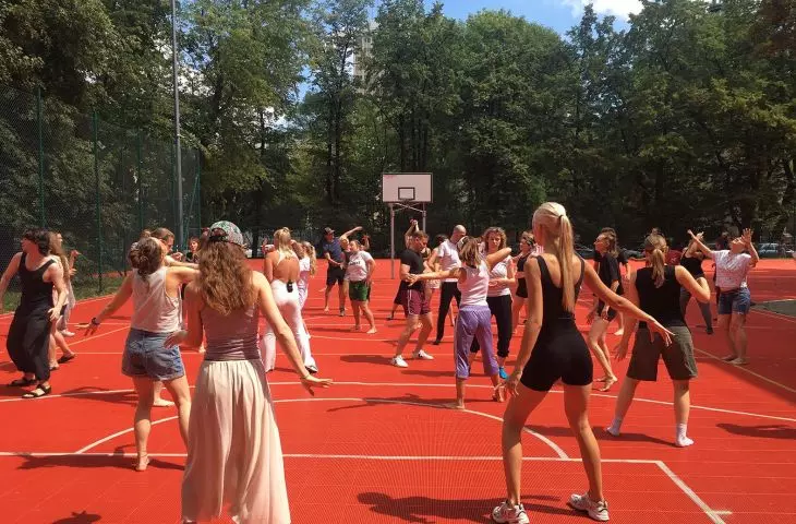 Zajęcia taneczne Marty Ziółek na boisku przy budynkach modernistycznych szkół