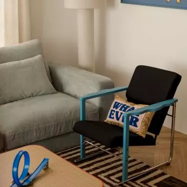 The calm, understated atmosphere of the living room is broken up by the blue of the armchair, the patterned rug, and whimsical details