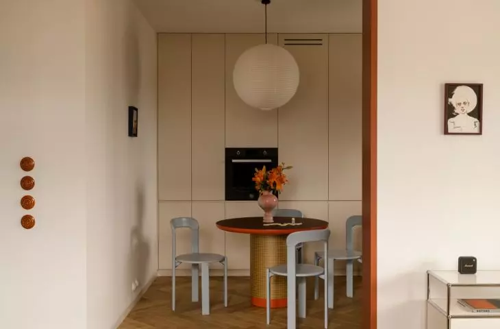 The dining room combines simple cabinetry with a round table, blue chairs, and a warm shade of orange 