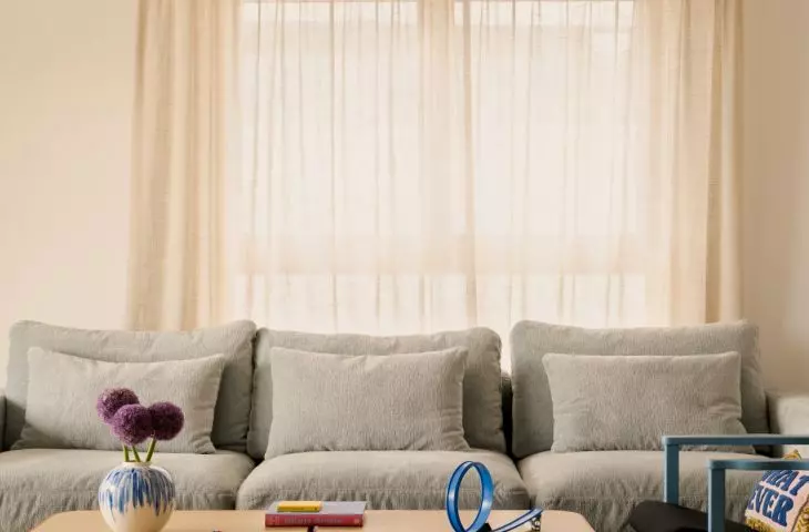 The living room's understated backdrop allows the bolder accents to stand out: the graphic rug, the blue armchair, and the colorful lamp