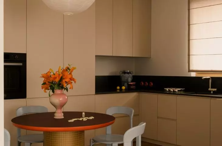 The kitchen features simple cabinetry, which is warmed up by wood, a round table, and orange accents