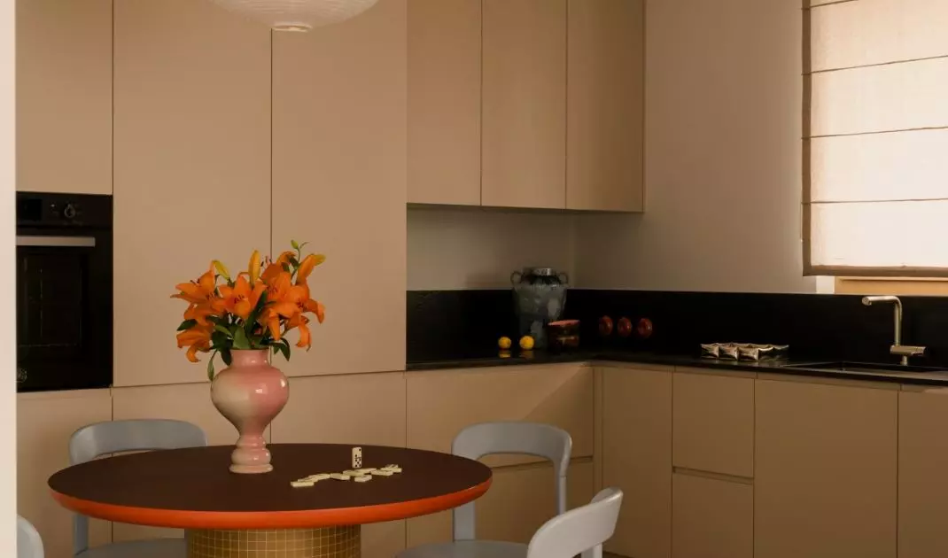 The kitchen features simple cabinetry, which is warmed up by wood, a round table, and orange accents