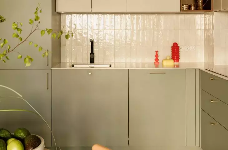 The green kitchen cabinets are accented with light-colored tiles and gold details