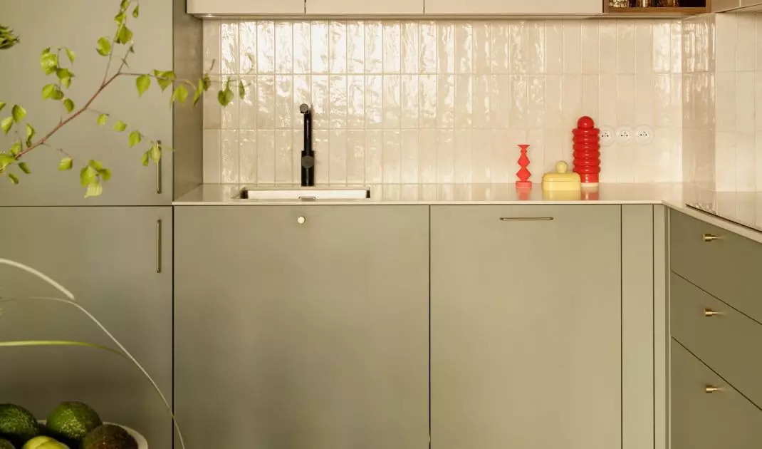 The green kitchen cabinets are accented with light-colored tiles and gold details