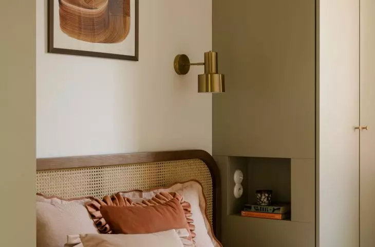 The artwork above the bed, the wicker headboard, and the gold wall sconce come together to create a warm, polished look in the bedroom