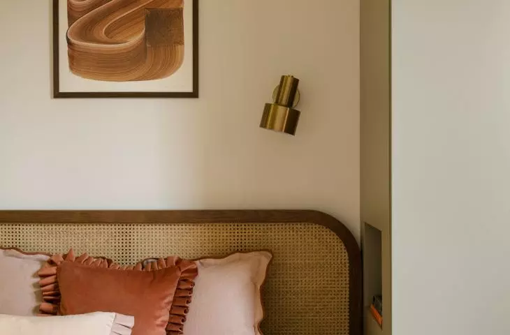 The artwork above the bed, the woven headboard, and the gold wall sconce come together to create a warm, polished look in the bedroom