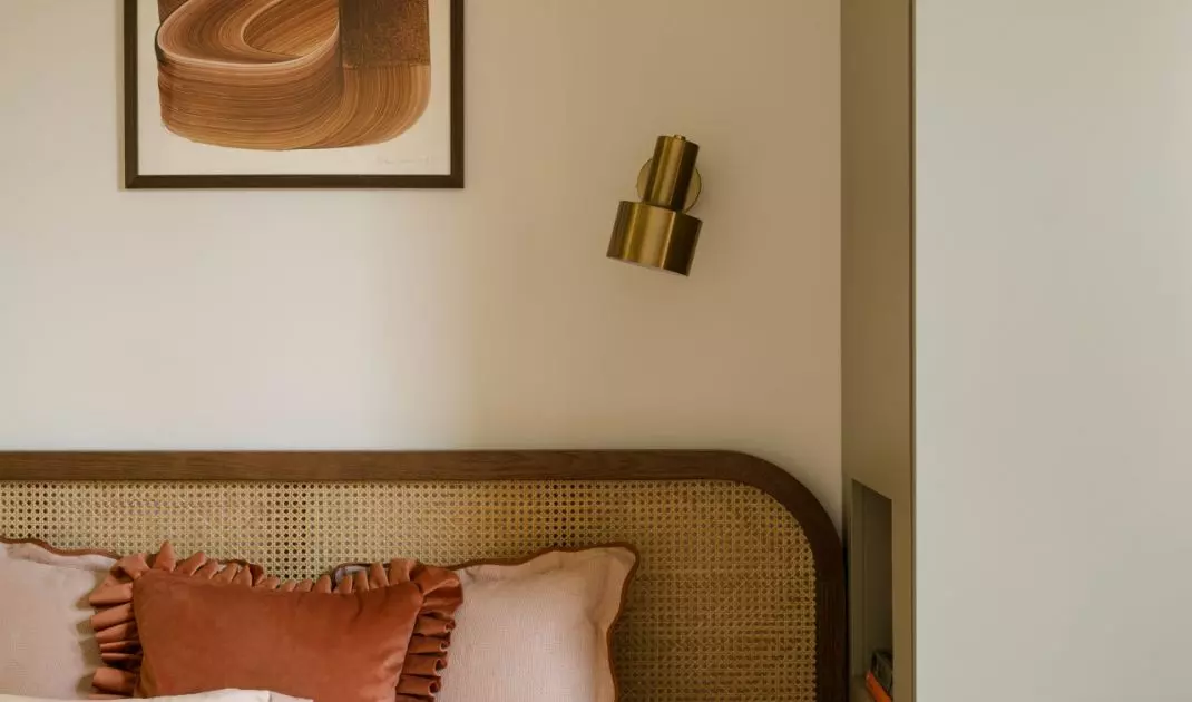 The artwork above the bed, the woven headboard, and the gold wall sconce come together to create a warm, polished look in the bedroom