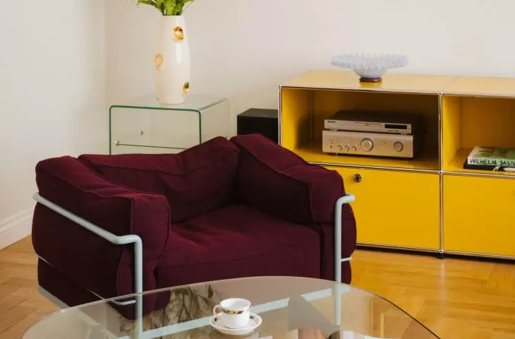 A burgundy armchair, a glass coffee table, and yellow cabinetry create an interior with character