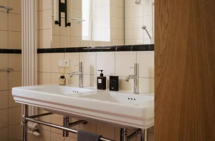 In the second bathroom, the retro style is reflected in the glossy tiles, steel accents, and wood, which adds warmth to the more graphic composition