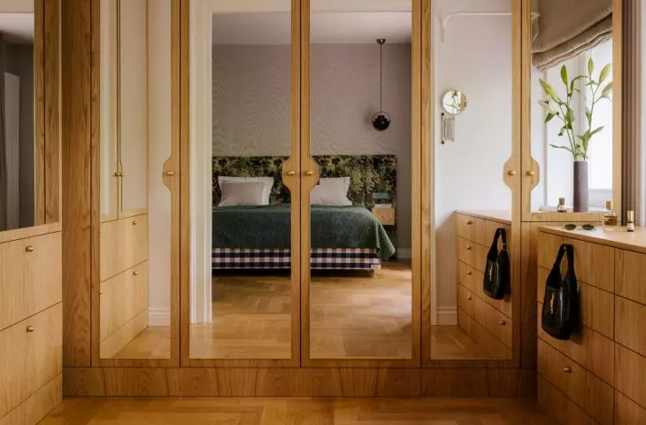 The wooden wardrobe with mirrored doors reflects light and the view of the bedroom, making the private area of the apartment seem more spacious