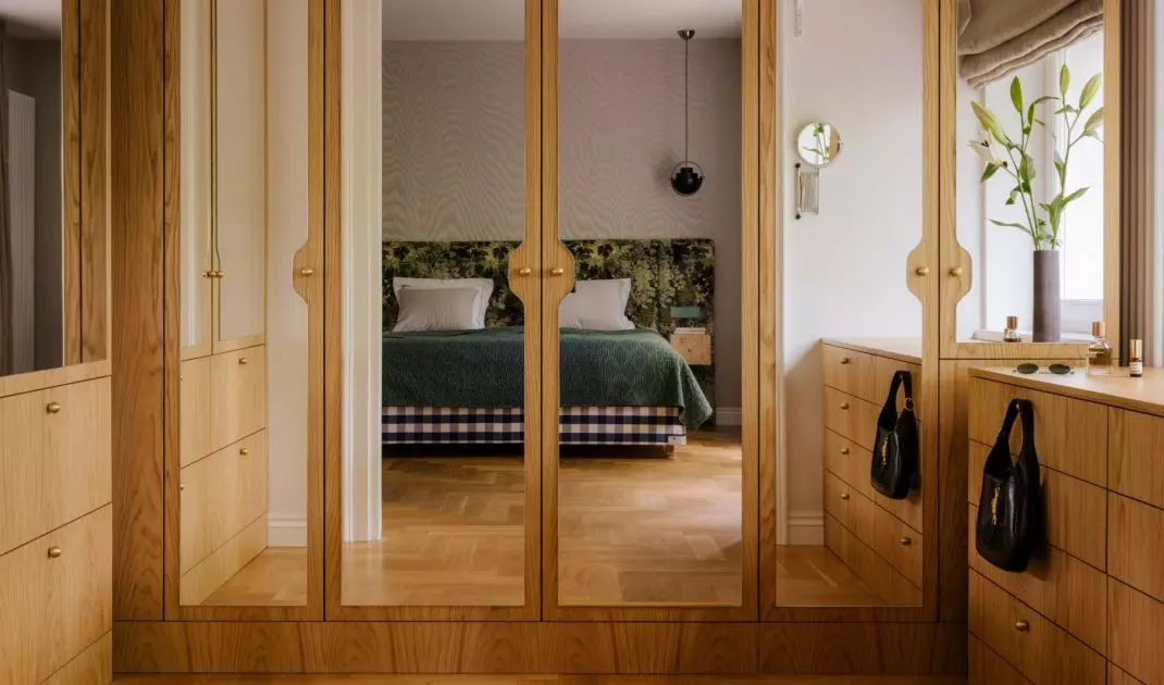 The wooden wardrobe with mirrored doors reflects light and the view of the bedroom, making the private area of the apartment seem more spacious