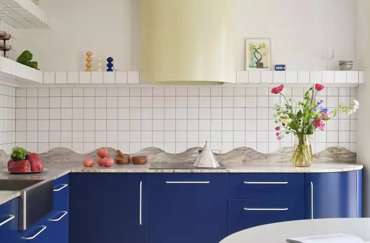 The blue kitchen combines the simple geometry of white tiles with the undulating line of the stone countertop