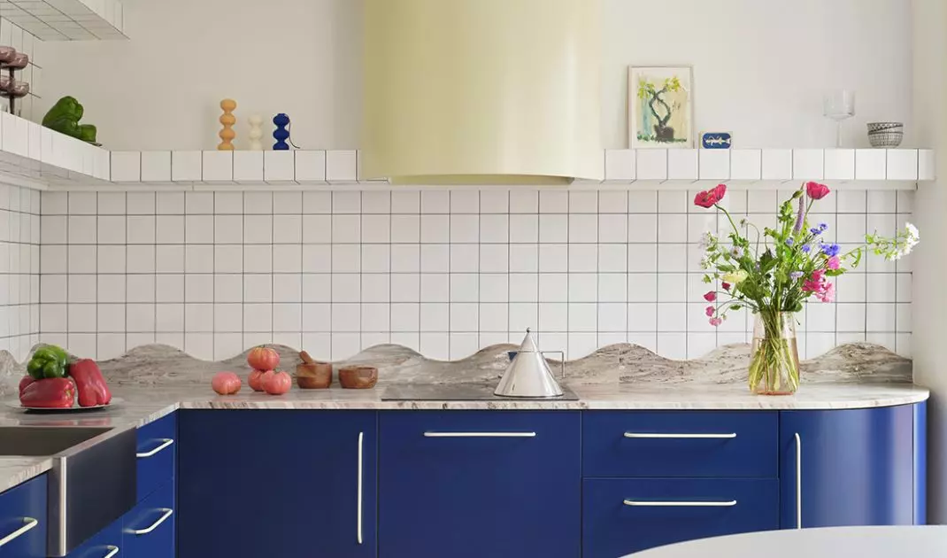 The blue kitchen combines the simple geometry of white tiles with the undulating line of the stone countertop