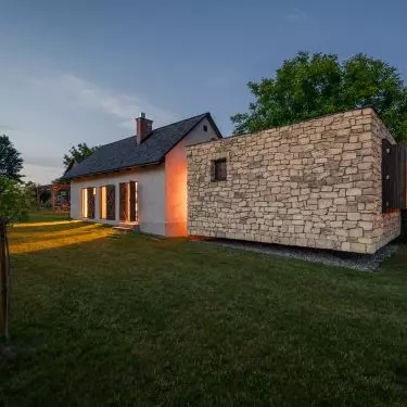 The former stable and the new stone structure come together in a single frame: plaster, wood, and stone create a serene blend of old and new