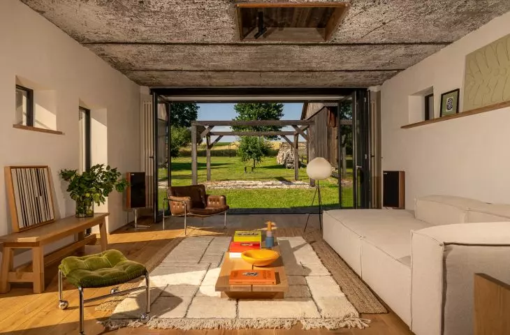In the living room, the exposed ceiling and brick wall contrast with a light-colored sofa, wood, and personal items, ensuring that the interior retains its homey warmth