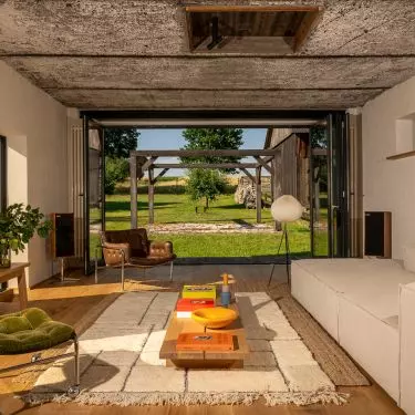 In the living room, the exposed ceiling and brick wall contrast with a light-colored sofa, wood, and personal items, ensuring that the interior retains its homey warmth