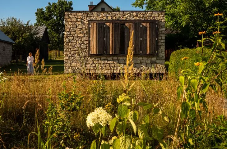 The stone structure does not dominate the garden—rather, it blends peacefully into the greenery, allowing it to soften the harshness of the material