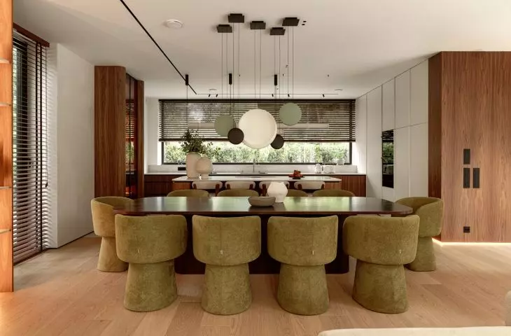 The open-concept living area combines the living room, dining room, and kitchen into a single elegant space featuring wood, stone, and olive-colored accents 