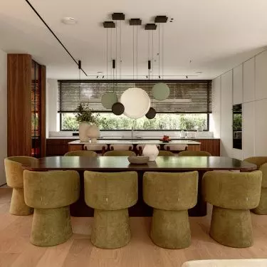 The open-concept living area combines the living room, dining room, and kitchen into a single elegant space featuring wood, stone, and olive-colored accents 