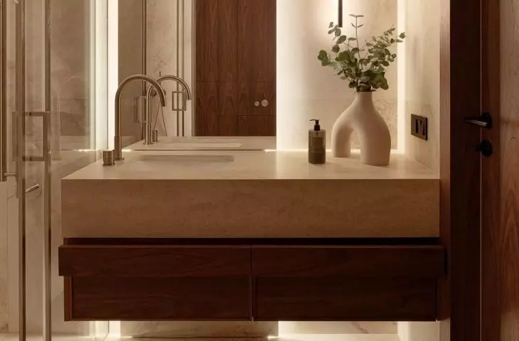The bathroom combines warm stone, wood, and mood lighting to create the atmosphere of a private spa