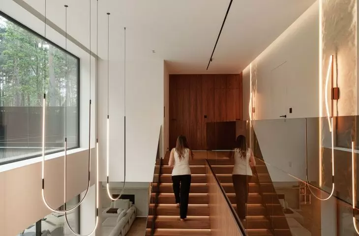 The staircase, with its wooden cladding, glass railing, and slender lamps, forms one of the most striking focal points of the house