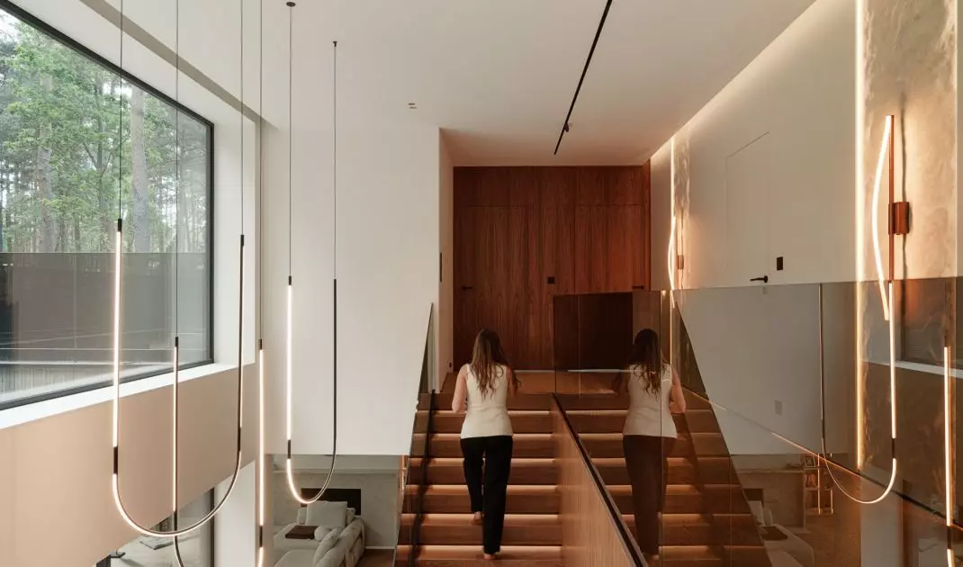 The staircase, with its wooden cladding, glass railing, and slender lamps, forms one of the most striking focal points of the house