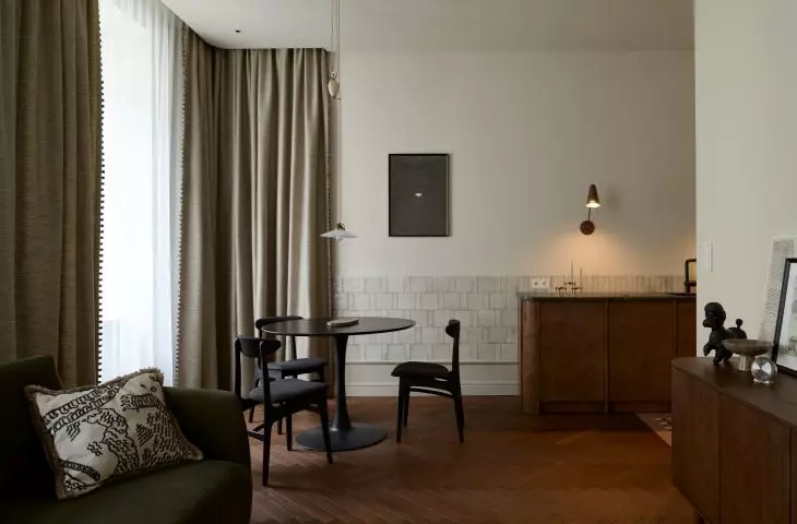 The living area of the Peachy Apartment combines the living room, dining room, and kitchen into a single calm, refined space. Warm wood, soft fabrics, and dark accents add contrast to the interior’s neutral palette