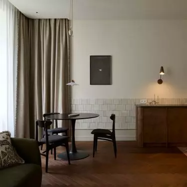 The living area of the Peachy Apartment combines the living room, dining room, and kitchen into a single calm, refined space. Warm wood, soft fabrics, and dark accents add contrast to the interior’s neutral palette