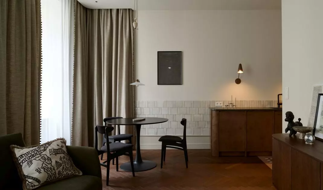 The living area of the Peachy Apartment combines the living room, dining room, and kitchen into a single calm, refined space. Warm wood, soft fabrics, and dark accents add contrast to the interior’s neutral palette