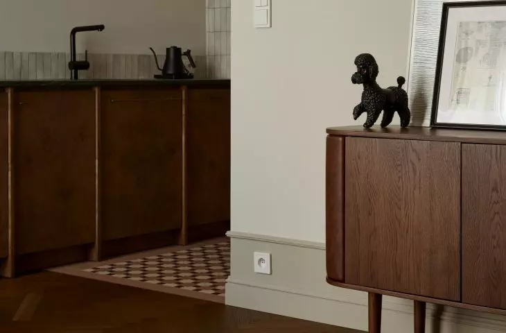 The kitchen and living room flow into one another here without a clear boundary. The checkered cabinet fronts, dark countertop, wooden dresser, and decorative accents create a cohesive, warm atmosphere in the interior.