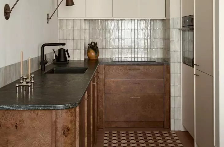 The kitchen was designed to be an elegant piece of furniture. The burl wood cabinet fronts, green stone countertop, and patinated details blend well with the apartment’s atmospheric character