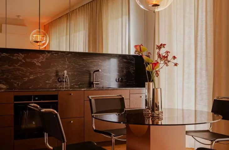 The kitchen and dining room are designed around the contrast between dark stone, wood, chrome, and soft curtains