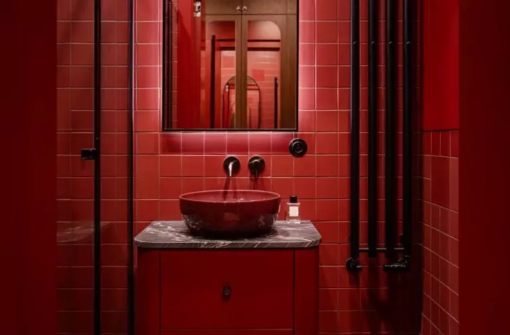 The small bathroom was designed with a bold approach: burgundy, black, and glossy finishes create an intimate, striking interior