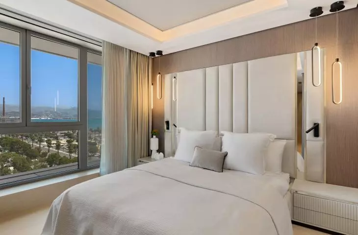 The master bedroom combines a soft, upholstered headboard, decorative lighting, and a view of the Mediterranean Sea