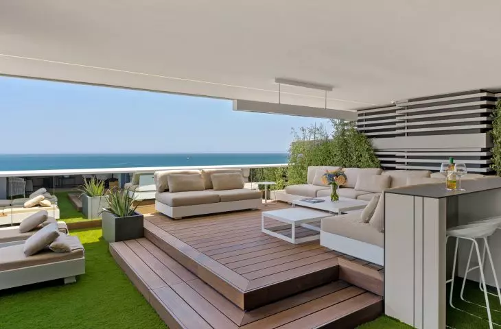  The terrace serves as an outdoor living room. A wooden deck, soft modular seating, and plants create a relaxing space with a view of the sea 