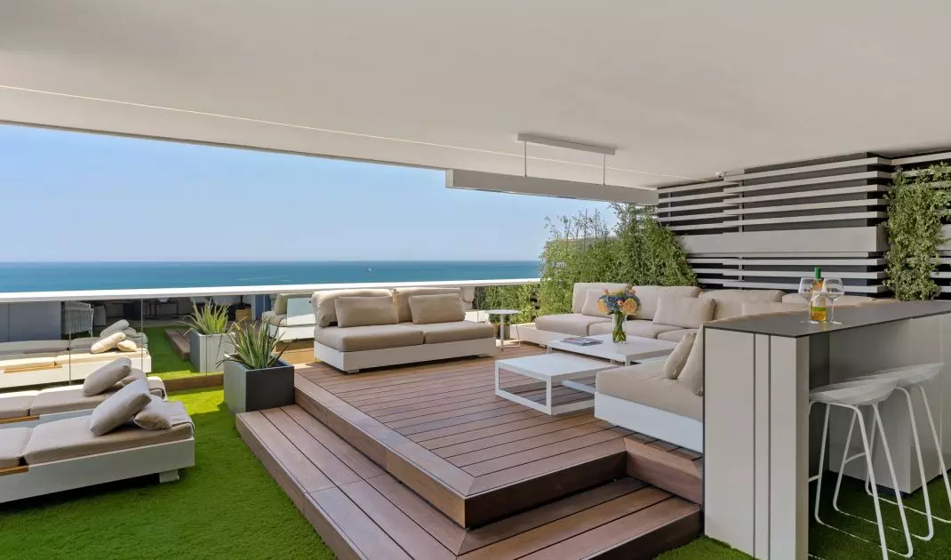  The terrace serves as an outdoor living room. A wooden deck, soft modular seating, and plants create a relaxing space with a view of the sea 