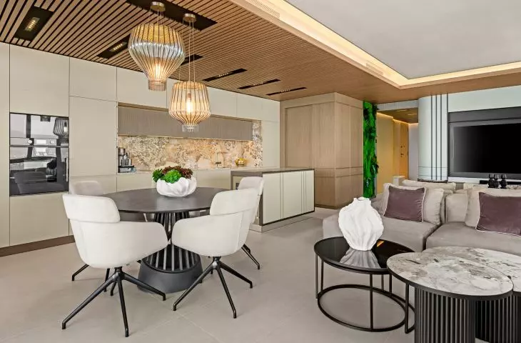 The living area combines the living room, dining room, and kitchen into a single open space. Quartzite, a wooden ceiling, and soft fabrics create the interior’s elegant, Mediterranean character