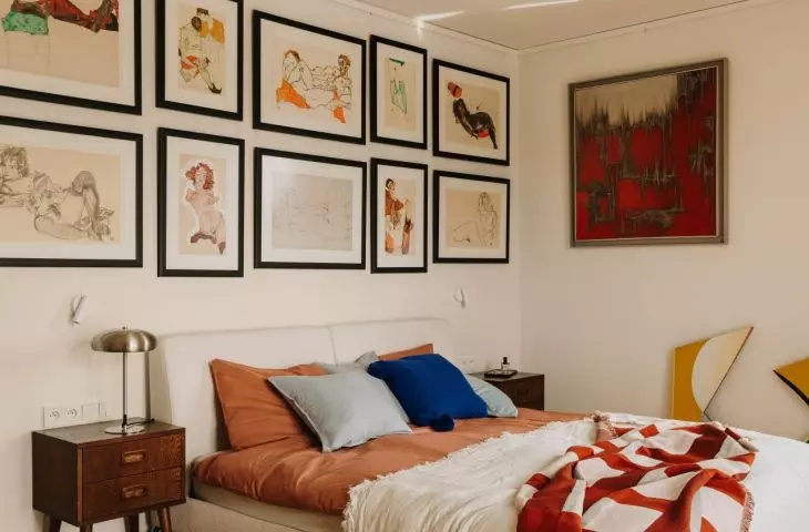 A gallery of paintings above the bed gives the bedroom a personal touch