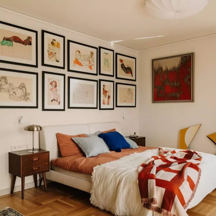 A gallery of paintings above the bed gives the bedroom a personal touch