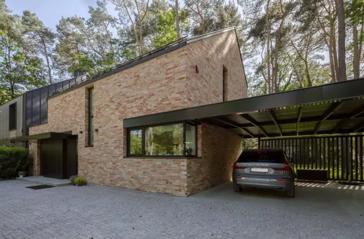 The brick structure is complemented by a lightweight, black carport with vertical slats