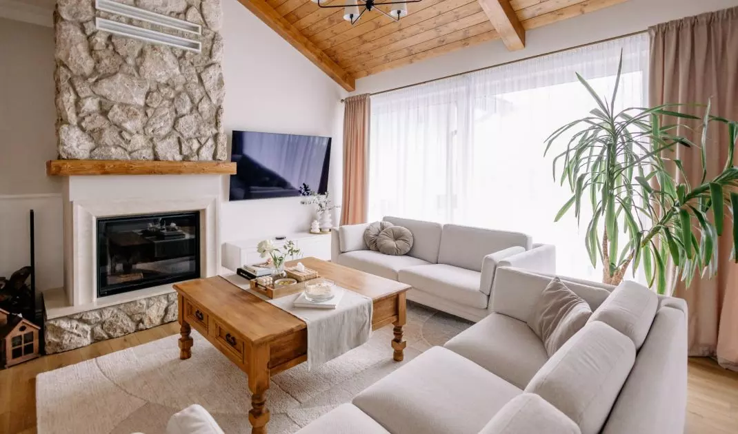 The living room features a high wooden ceiling and a fireplace finished with natural stone