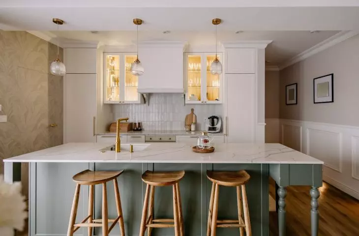 The olive-colored island breaks up the light, symmetrical kitchen cabinetry and serves as one of the interior’s strongest color accents