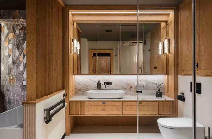 One of the bathrooms combines wooden cabinetry with light-colored stone, a large mirror, and glass partitions