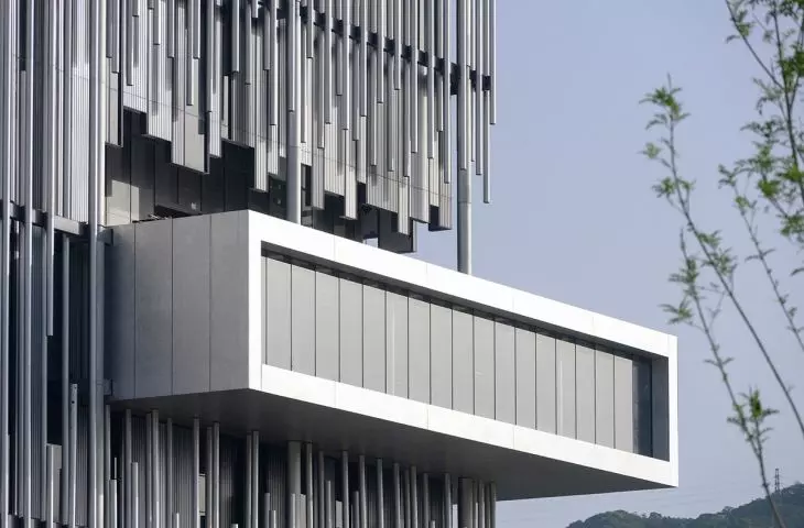 The gallery's protruding structure cuts across the facade, which is composed of vertical aluminum elements resembling a silvery reed bed